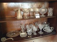 Full view of all cut glass and stemware items on two shelves including stemware glasses, candy dish with lid, sugar bowl, decanter, and small decorative pieces.