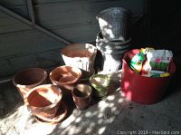 Overall view of terra cotta pots, decorative urns, and red basket with garden supplies in sunlight.