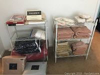 Photo showing two metal 3-tier shelving units filled with various linens and bedding items, shelving only for sale.