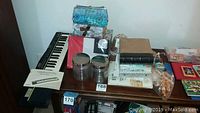 Overview of table with Casio keyboard, manuals, photo albums, trinket boxes, and containers