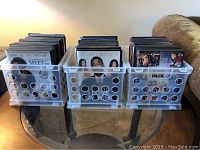 Three clear plastic crates filled with upright DVD cases on a glass table