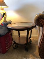 Lightly used round two-tier side table with cherry wood finish, inset glass top, metal scroll legs with leaf detail.