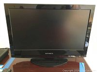 Front view of black Dynex 24 inch LCD TV on a stand, screen off, visible Dynex logo on bezel.