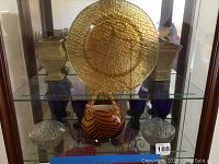 Glass display cabinet shelf showing amber glass plate and vases on upper shelf, blue goblets on shelf below.