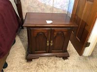 Front view of solid cherry wood end table with closed cabinet doors showing brass-tone hardware and decorative carved wood doors.