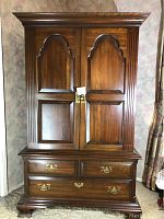 Front view of closed cherry wood armoire showing two paneled doors, crown molding and lower drawers