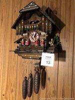 Overall front view of wooden chalet-style cuckoo clock with three pinecone weights hanging