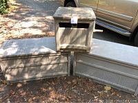 Three items shown outside on ground by vehicle: two large storage bins and one garden hose reel.