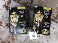 Two boxed new solid brass outdoor motion sensing coach lights by Hampton Bay, showing front packaging with product image and branding.