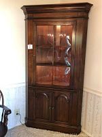 Full front view of closed cabinet showing hardwood finish, glass-pane upper door, crown molding and lower doors.