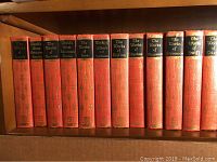 Shelf view showing volumes with red covers and gold embossed spines with dark title labels, mainly showcasing works by authors including Lamb, Kipling, Stevenson, Swift, and Goldsmith.