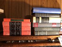 Top view of two stacks of hardbound books on a bookshelf, showing spine titles and colors including red, blue, white, and gray with classic literature titles.