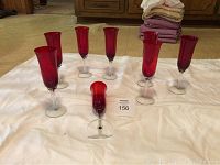 Eight red glass champagne flutes arranged on a white sheet showing the red bowl and clear stem and base.