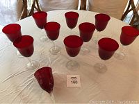 Overview photo showing eleven red water glasses arranged on a white tablecloth with one glass tipped over.