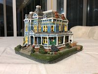 Detailed front and side views of the miniature Queen Victoria lighted house showing Victorian style architectural details, painted windows, and landscaping on a solid base.