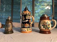 Three German beer steins placed on white tablecloth, different sizes and styles, with natural background light
