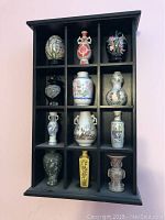 Photo of the entire black wooden wall-mounted display with twelve compartments, each holding a small urn