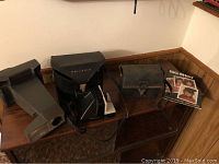 Image showing seven assorted cameras including three Polaroids with cases and accessories arranged on a wooden cabinet surface.