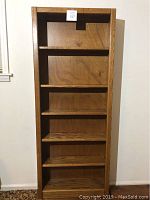 Front view of an oak wooden bookcase with six shelves showing the entire height and width.