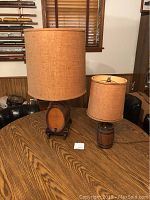 Two barrel style table lamps with burlap shades on a wooden table, showing size difference.