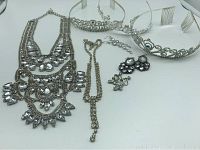 Lot of jewelry including two rhinestone necklaces, three pairs of rhinestone screw-back earrings, and three rhinestone princess crowns on white background.