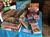 Photo showing multiple vintage games including Cheers, Battleship, Clue, Christmas Dominoes, Waterworks, and various card decks arranged on table.