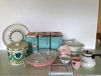 Front view showing all items on display including canisters, kettle, casseroles, cups, tin, and plate