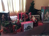 Table with various Christmas decorations including wreath, small Christmas tree, Santa figurines, candles, and boxes.