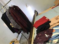 Seven wool sweaters shown hanging on a rod and folded on a table including a distinctive red and black Norm Thompson cardigan sweater, various colors like black, maroon, beige, and a light blue sweater vest.