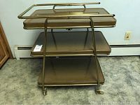 Front view of vintage metal rolling cart showing three shelves and caster wheels.