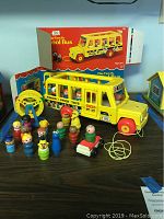 Wide view showing the Fisher Price yellow school bus, assortment of wood and plastic figures, small toy car, Ferris wheel accessory, and original box in background.