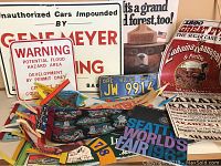 Photo showing several vintage travel pennants, license plates, and signs including flood hazard warning sign, Gene Meyer impound sign, and event posters.