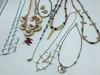 Overview of all jewelry including 8 necklaces and 4 earrings displayed on white background showing variety of ethnic style necklaces, some with bird charms, shell beads, and red accents.