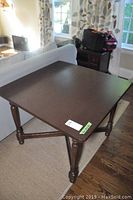 Front angled view of dark oak card table showing surface and leg structure with wear and scratches.