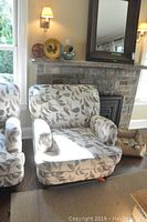 Two leaf-pattern upholstered armchairs side by side in living room near brick fireplace and mirror.