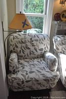 Front view of armchair in corner showing leaf patterned upholstery and rolled arms