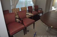 Seven dining chairs, five in red and gold striped upholstery and two in gold-tone paisley upholstery, arranged near a wooden dining table in a room with window curtains.