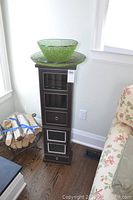 Full view of brown wooden tower shelf with four drawers and in-use green beaded wire bowl and tray on top, hardwood floor background