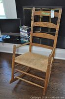 Wooden rocking chair with ladder back and woven seat, slight wear visible on wood surfaces, shown from front angle.