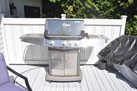 Front angled view of the Blue Ember stainless steel BBQ grill showing three control knobs, hood with temperature gauge, side shelves, and two-door storage cabinet.