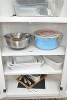 Photo of shelves containing 3 stainless steel mixing bowls, 5 plastic mixing bowls in packaging, and 4 white rectangular ceramic baking dishes.