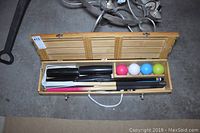 Wooden croquet set open showing four colorful balls, mallets, and wickets inside light wood carrying case.