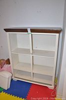 Front view of wood TV cabinet with white body and natural wood top. Shows four open shelves and central vertical panel with lock mechanism.