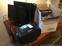 Two Dell monitors, Sony CD player/iPod dock, and box of assorted DVDs on wooden table