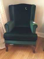 Front view of the green wingback chair showing its high back and plush cushioned seat with armrests.