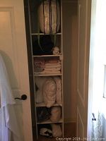 Shelving unit with various stacked linens including pillows in storage bags, folded sheets, and blankets.