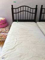 Single black wooden headboard on a bed frame with a mattress covered in a white protective cover. Wooden floor visible beneath.