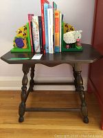Small dark wooden table with turned legs, holding children's books between sheep-themed bookends.