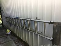 Full view of the aluminum extension ladder leaning against a wall, showing its length and dual-section design.