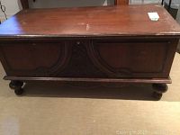 Front view of wooden cedar chest showing carved decorative front panel and bun feet.